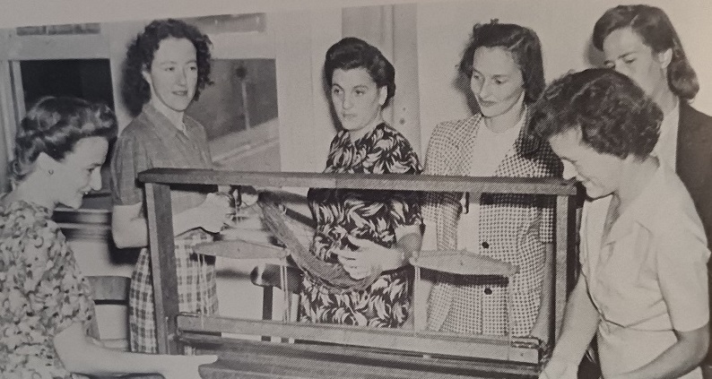 Six women gathered round a loom