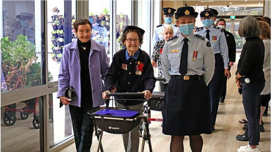 Elderly woman wearing medals flanked by RAAF personnel