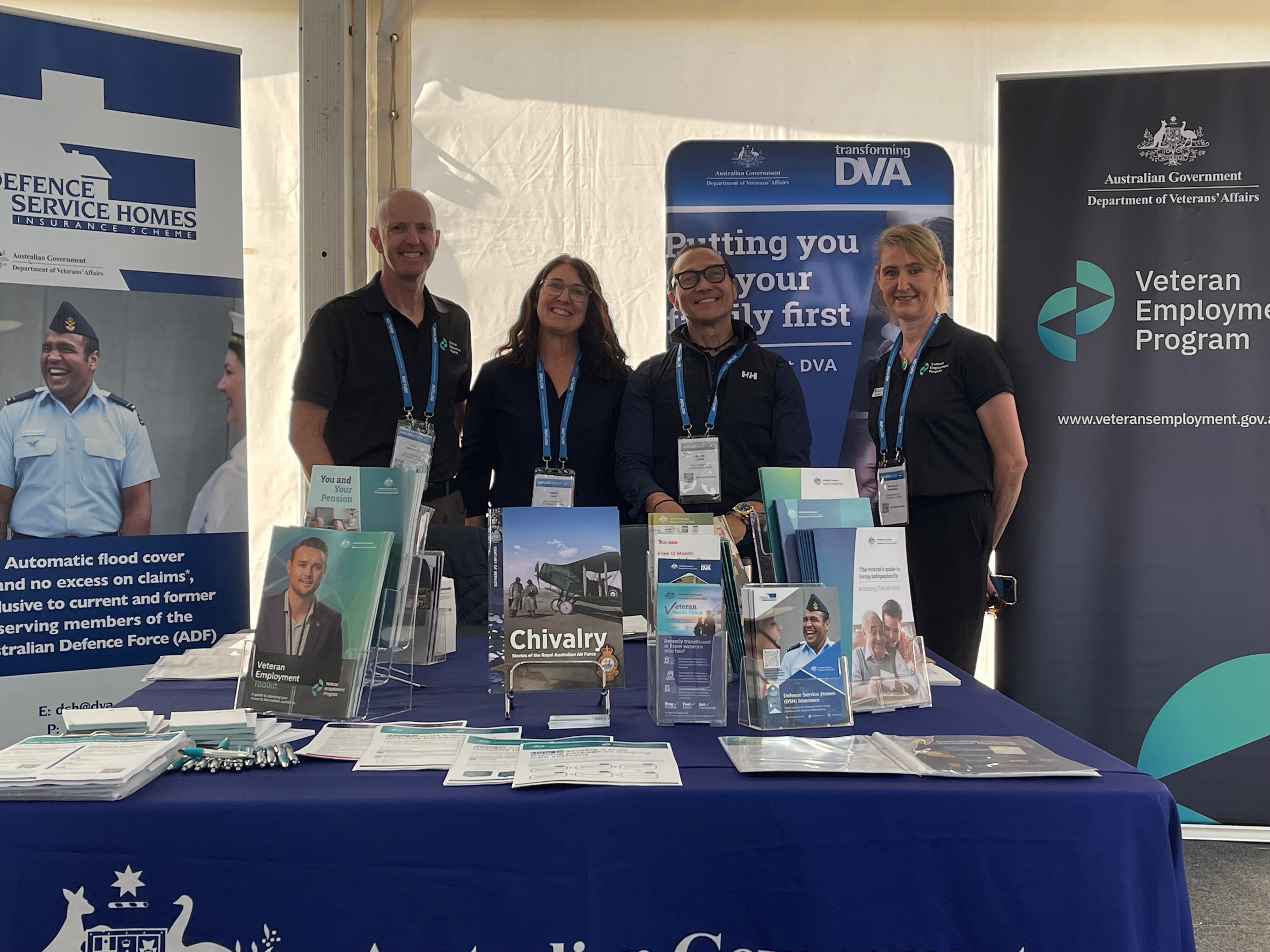 Two women and two men stand behind table with pamphlets and booklets to support veterans and their families