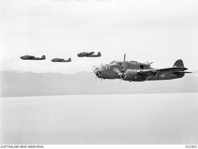 Aerial photo of four medium sized bombers flying above the sea with coast in background