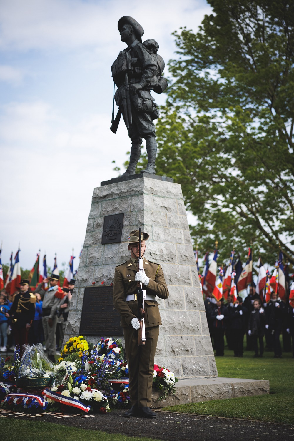 Bronze statue of First World War digger on high plinth, with Australian soldier standing in attention and crowd in background