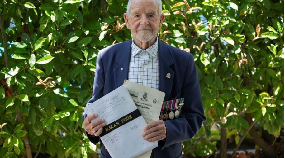 Older man poses for camera holding documents
