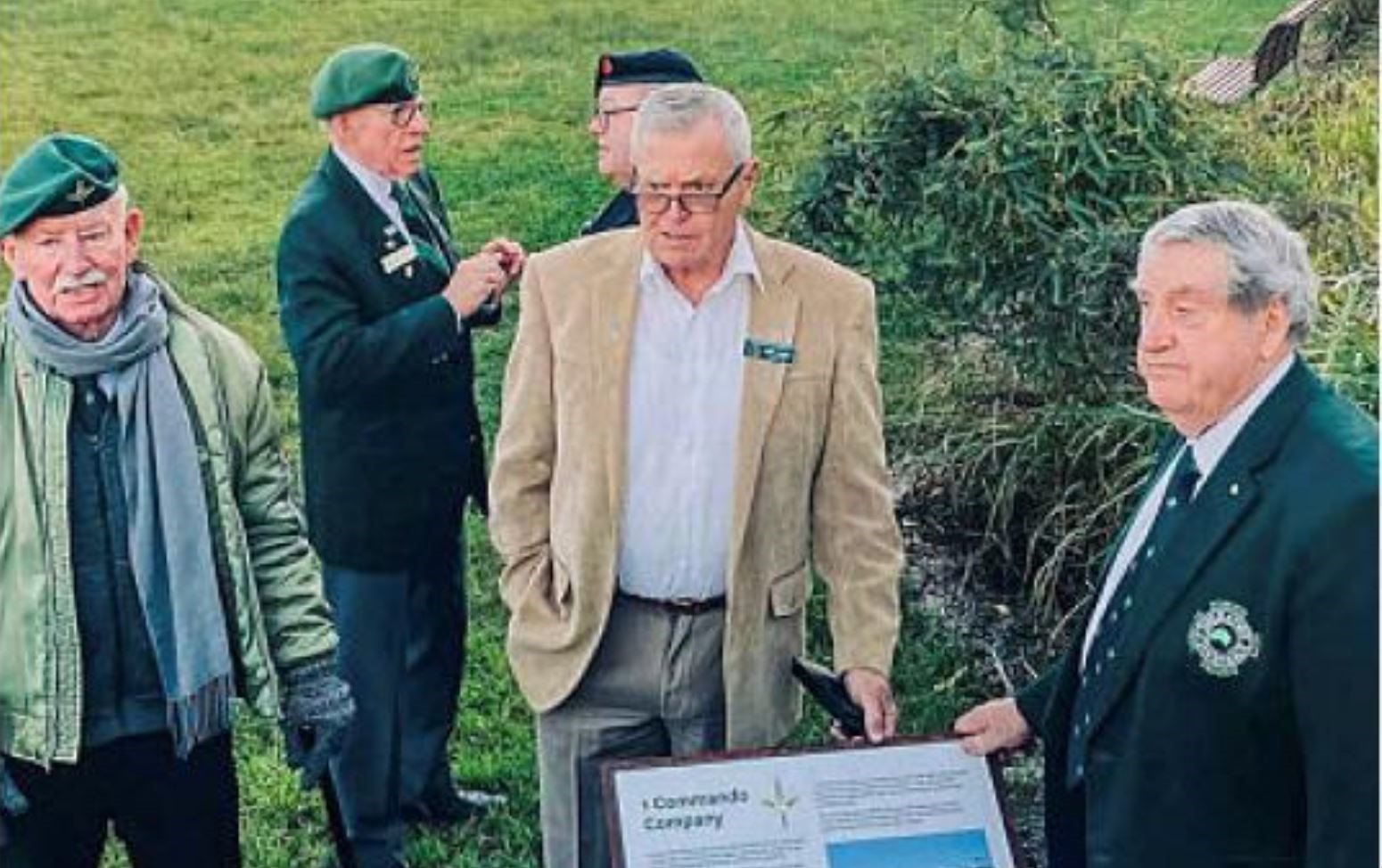 Six older men standing by plaque 