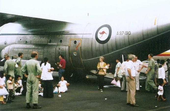 RAAF personnel and civilians stand beside small children on tarmac next to Hercules aircraft