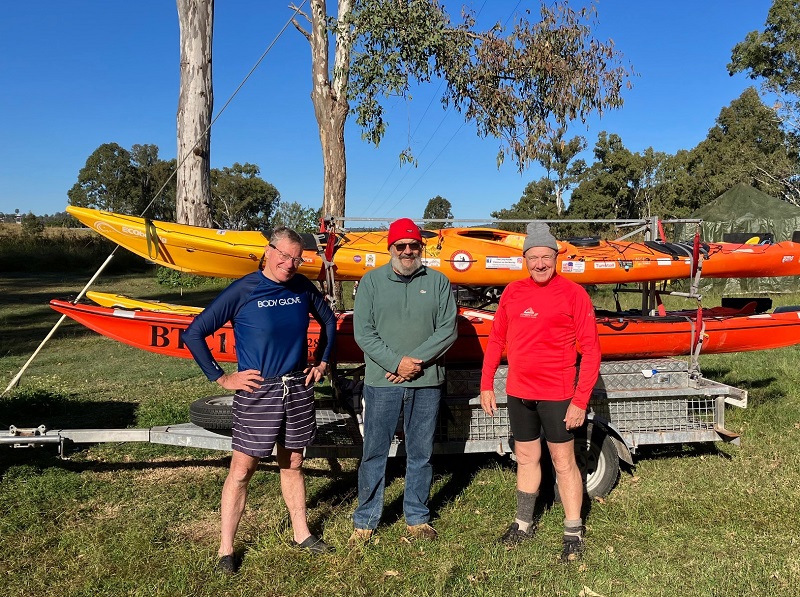Three men posing in front of kayaks on land