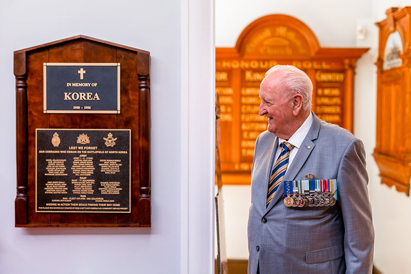 A photo of a older veteran in a suit with medals looking at a Korean War memorial