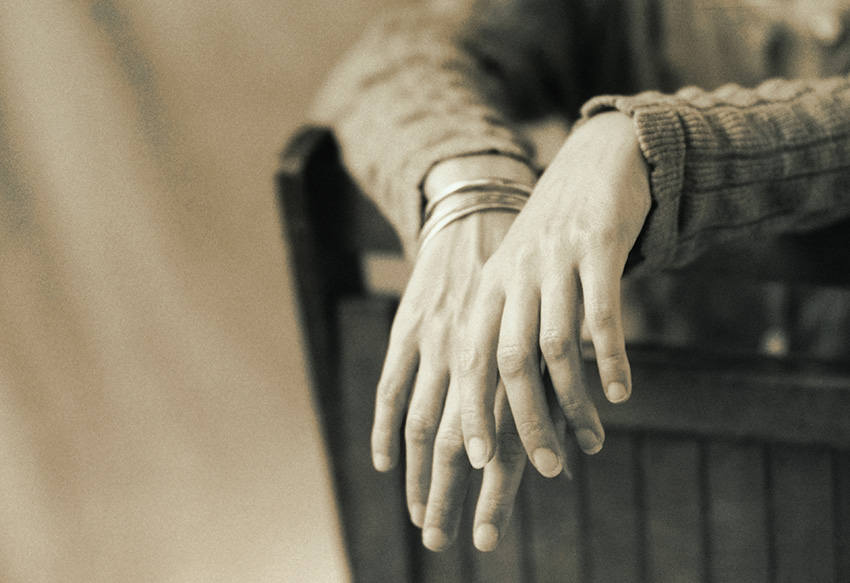 Two arms draped over a chair. The hands are close-up and in focus