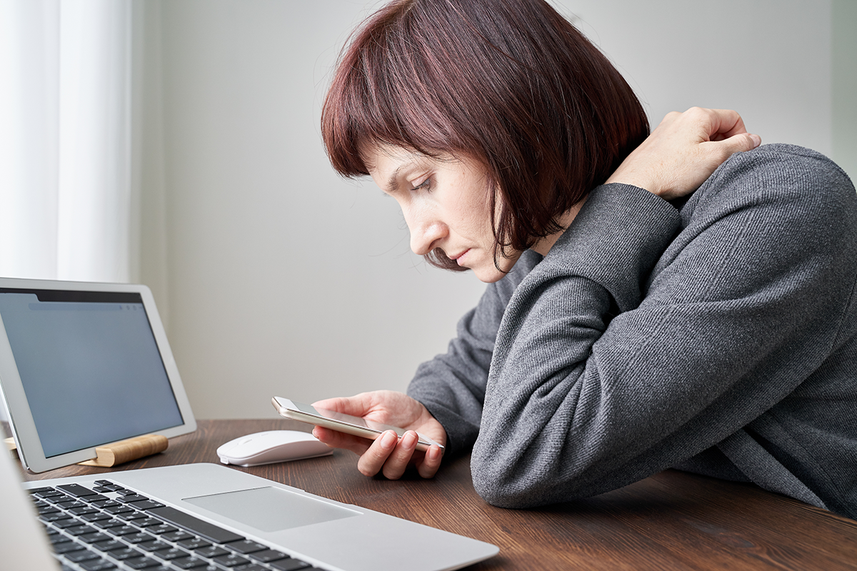 A woman is looking at her mobile phone in front of her computer.