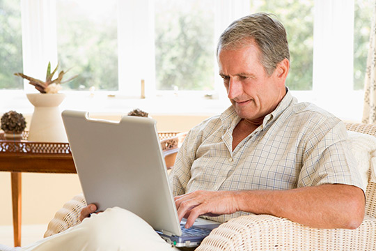 A baby boomer man, using a laptop computer whilst sitting in an armchair.