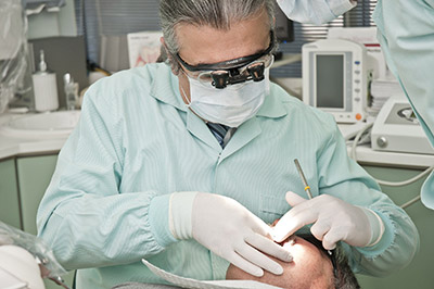 A dentist and their patient. The dentist is wearing a face mask and special magnifying glasses.