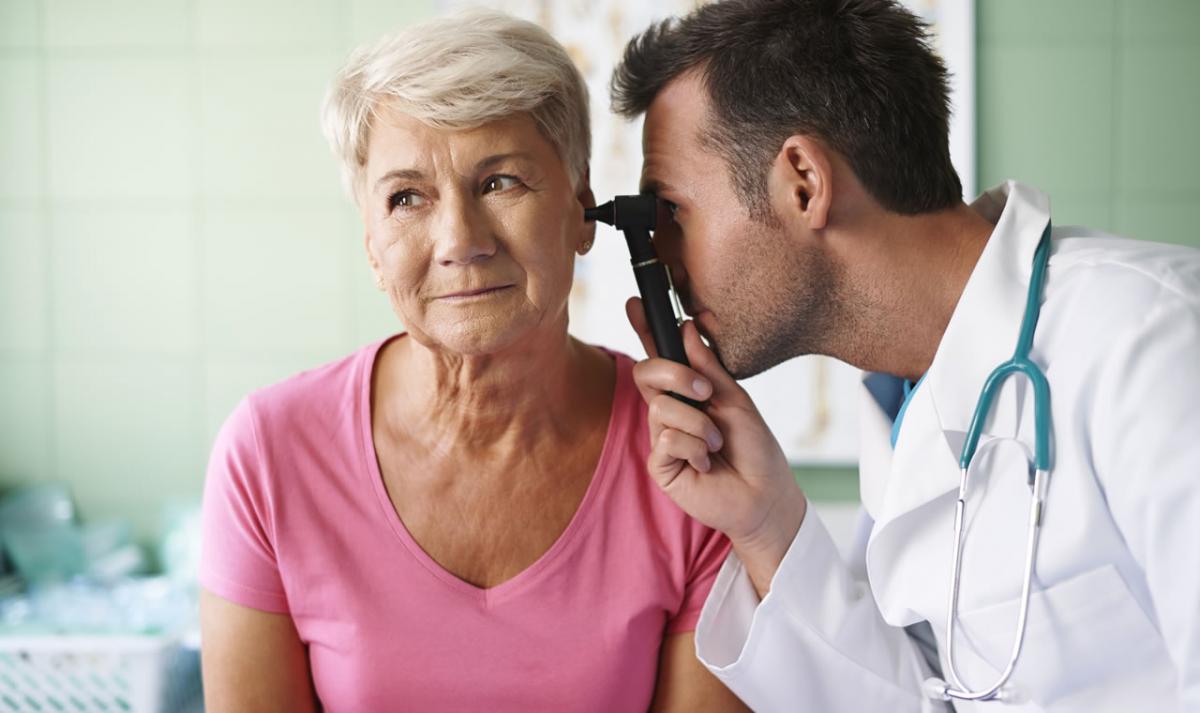 An audiologist (hearing medical doctor) inspects an elderly woman's ear with an otoscope