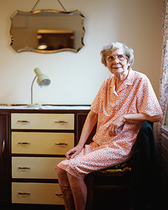 Elderly lady sitting by a chest of drawers