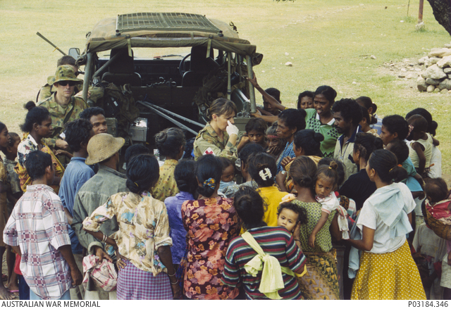 A crowd of Timorese gathered around a female medic as she points to her eye, trying to communicate with a Timorese patient in a medical clinic run from the back of an Australian Army land rover.