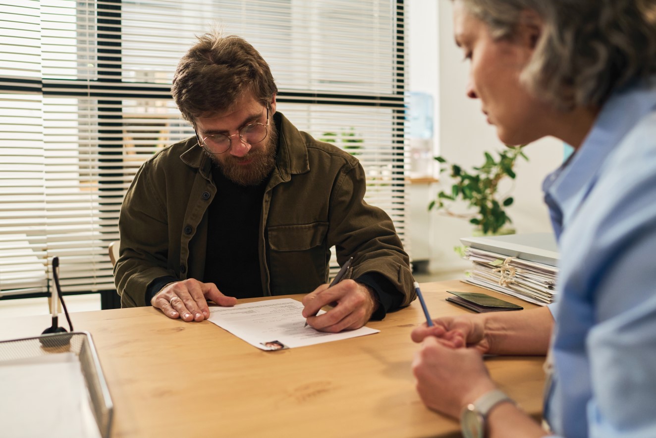 Professional woman helping middle aged man to fill out paperwork. 