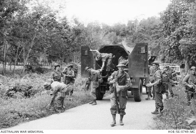 Soldiers alight from an armoured truck on a road.