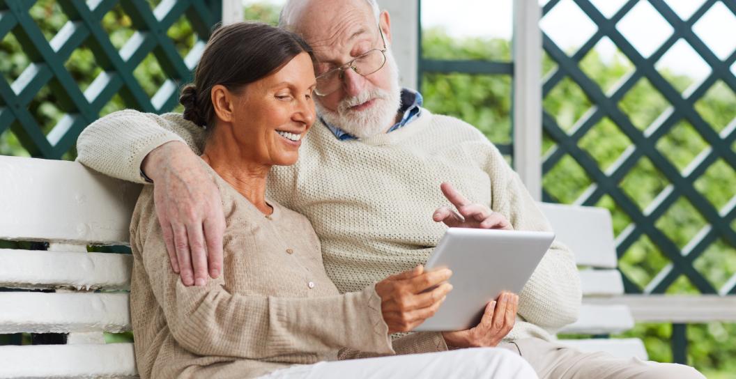 A retired woman and man are seated on a wooden bench and are looking at a notebook