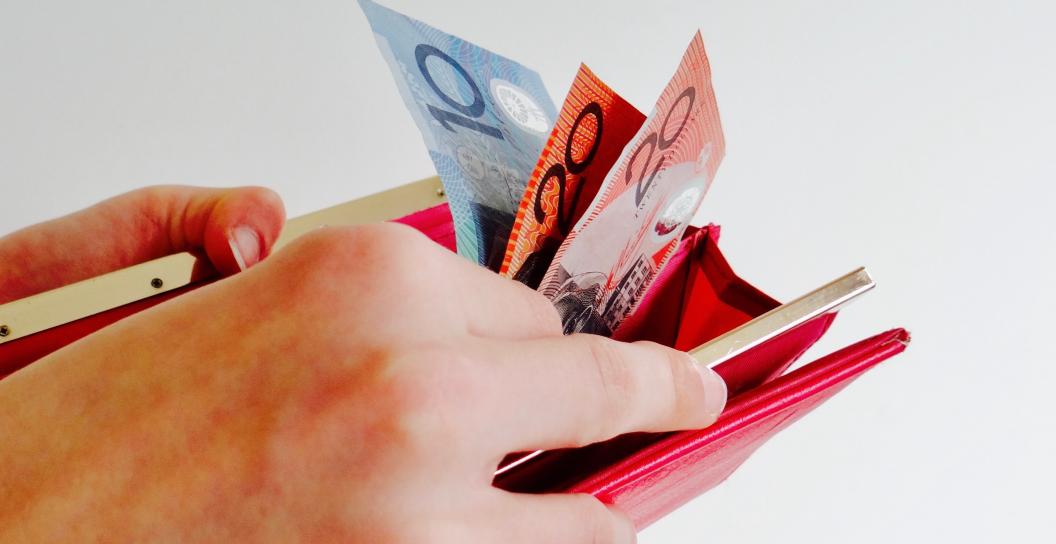 A hand is holding an open wallet and they are removing some Australian currency from the wallet