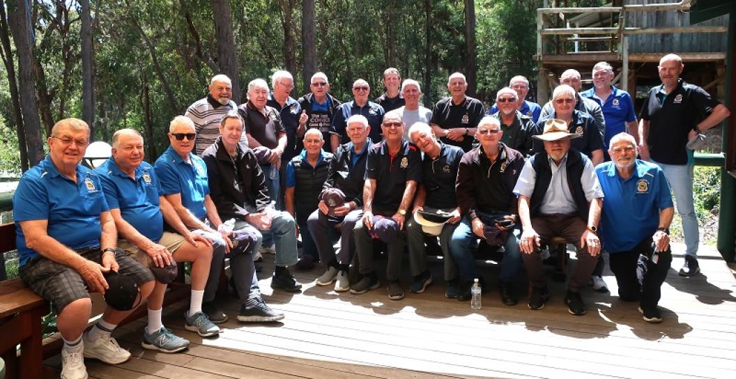 About thirty older men pose for photo on timber deck