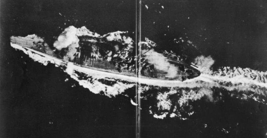 Aerial photo of battleship with smoke billowing from various sections of it