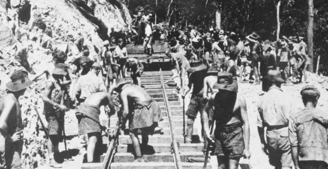 A black and white photo of Japanese prisoners of war working on the Burma-Thailand Railway. Several workers are laying railway track. Image Credit Australian War Memorial P00406.034