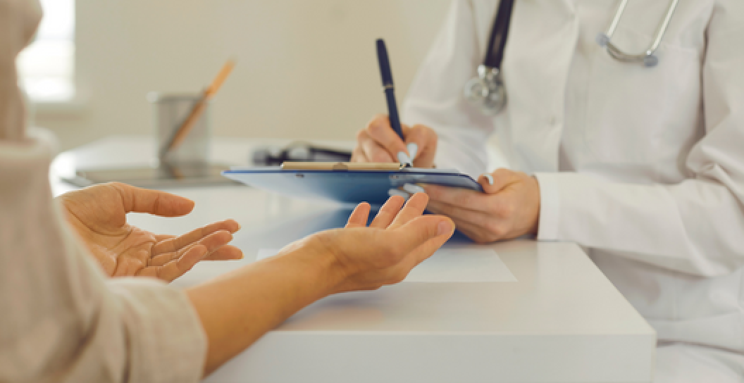 A general practitioner writes on a clipboard while meeting with a patient.