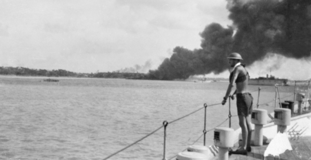 An unidentified sailor on board HMAS Platypus watches smoke bollowing from MV Neptuna after she was destroyed during the first Japanese air raid on Darwin.