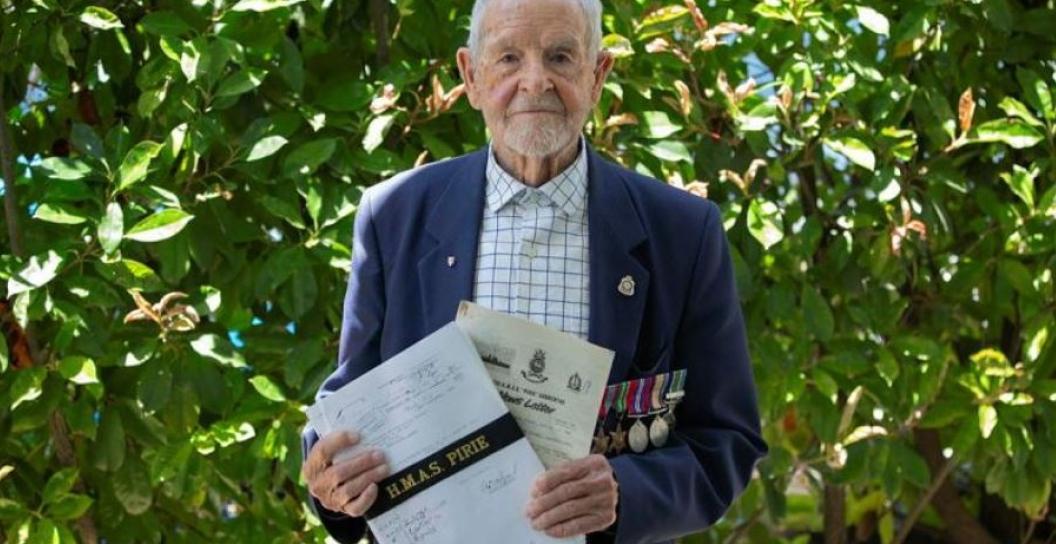 Older man poses for camera holding documents