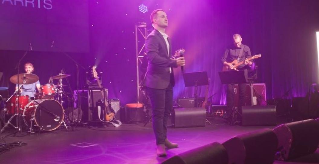 Man standing on stage with microphone with musicians in background