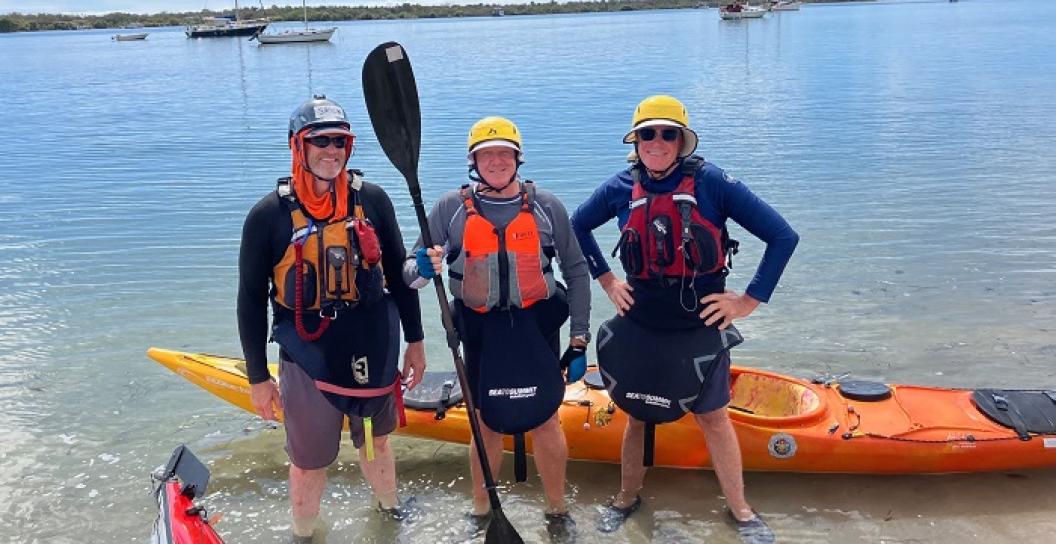 Three men posing in front of kayak at end of river