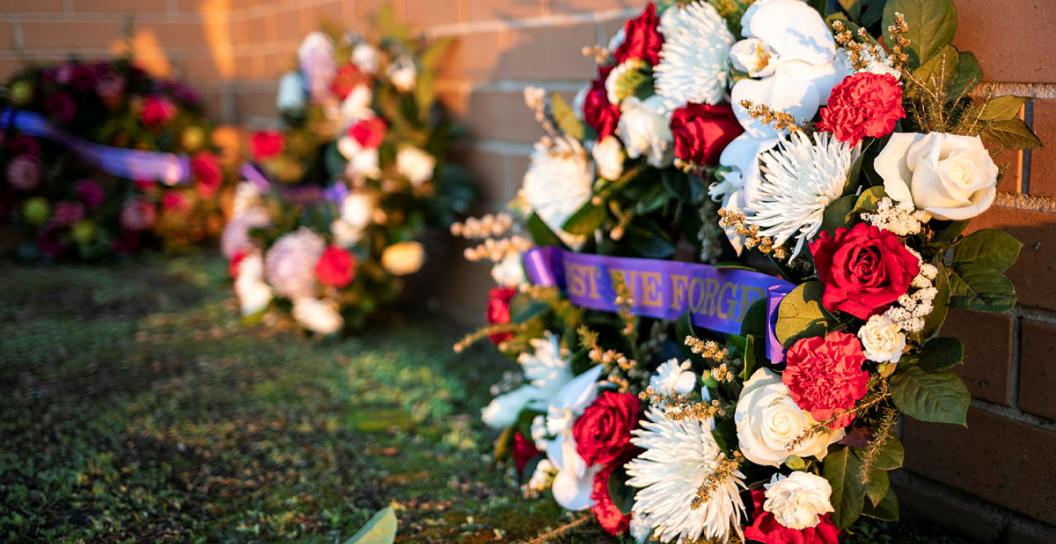 A wreath lays against brickwork at an Anzac Day memorial. Two additional wreaths stand beside it out of focus