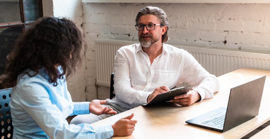 Man in white shirt taking notes, sitting next to lady in blue shirt.