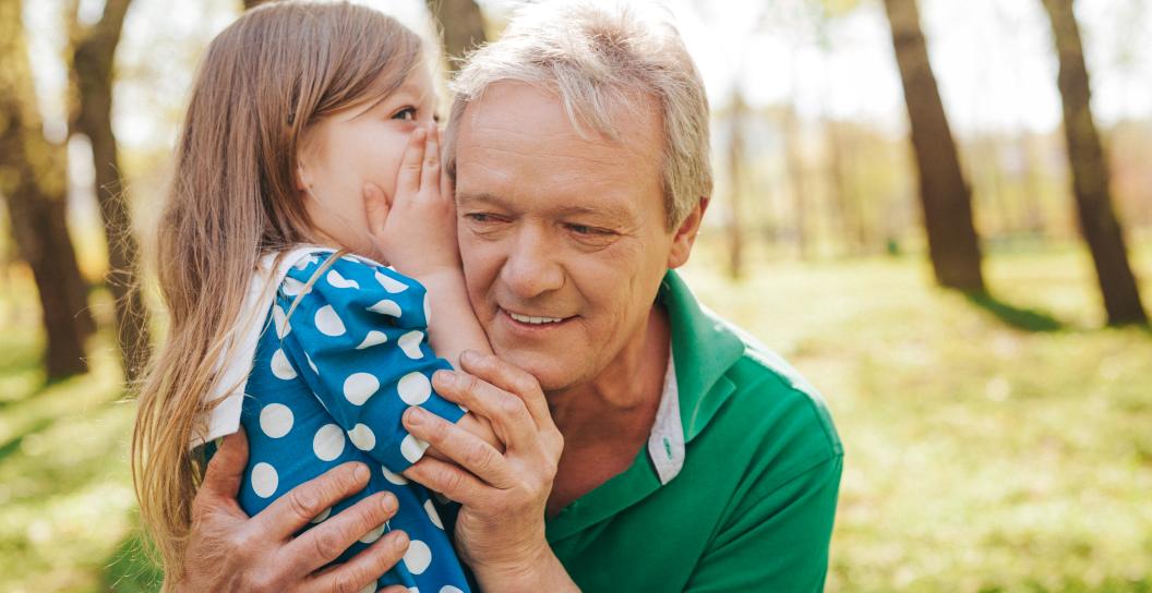 Little girl in blue dress whispers into elderly man's era