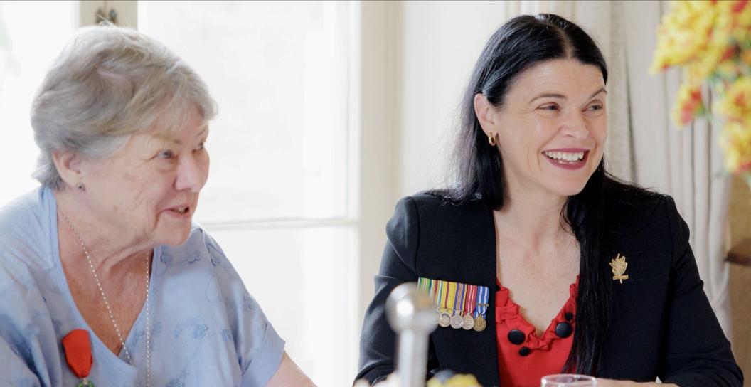 Two women, one older, one younger, seated at a dining table and smiling