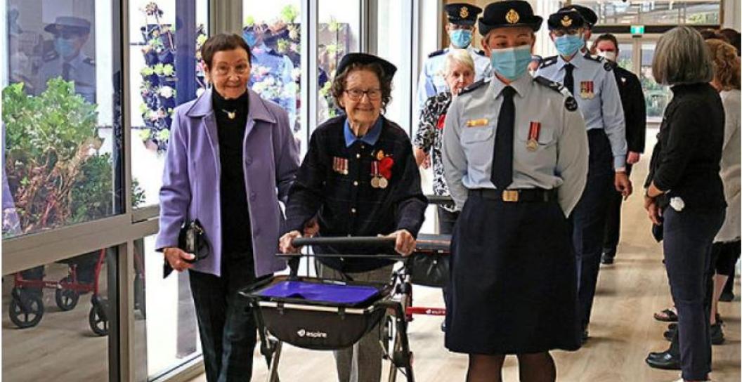 Elderly woman wearing medals flanked by RAAF personnel