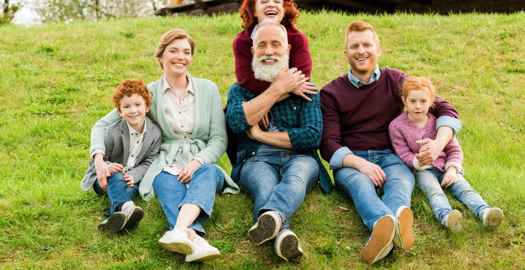 happy, multi-generational family sitting side by side on grass hill