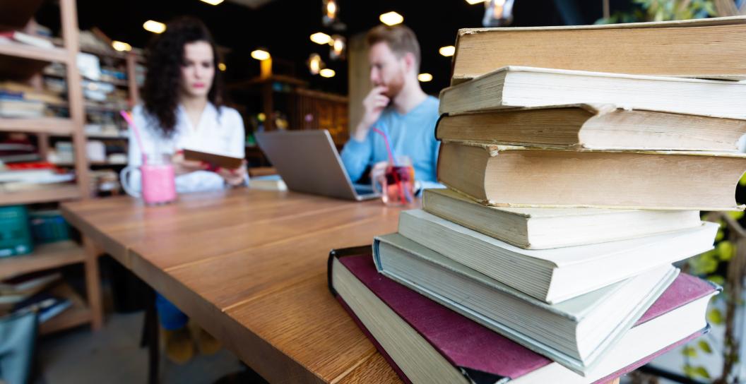 Stack of books on a table that two students are studying at