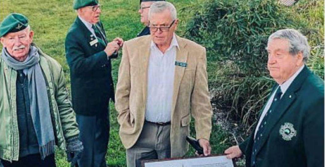 Six older men standing by plaque