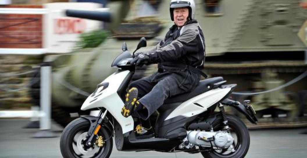 Older man on scooter riding past a tank