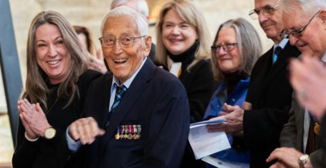 Elderly man wearing medals and smiling, surrounded by others outside a church