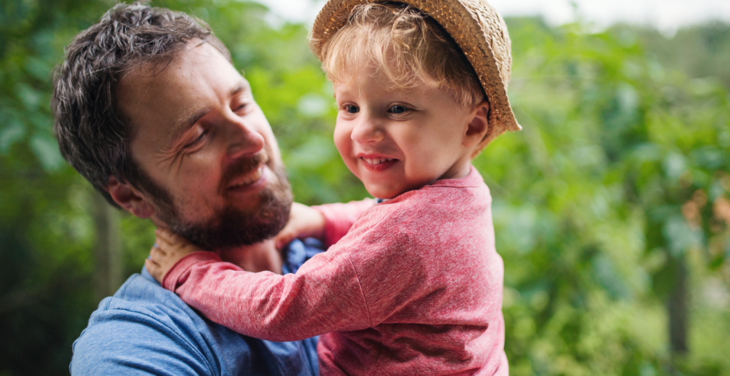 A man holds his young child, both are smiling