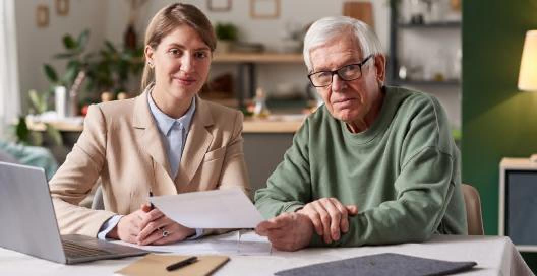 A young woman with an older man with paperwork in front of a laptop