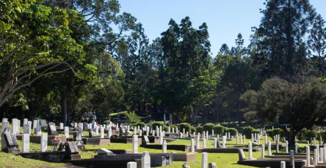 Toowong Cemetery showing headstones and graves against a blue sky with trees in the background