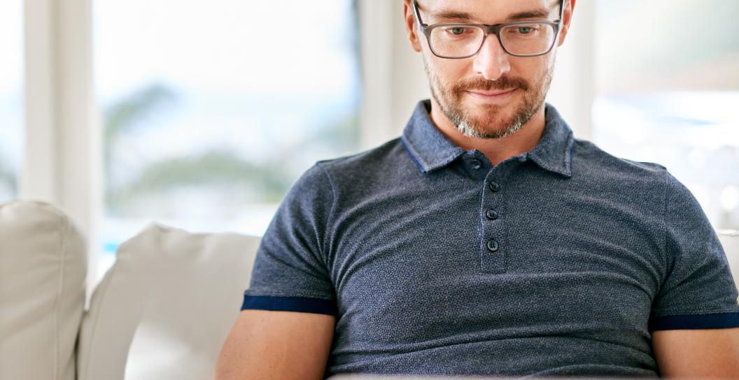 A white man sits on his couch with a laptop open on his lap