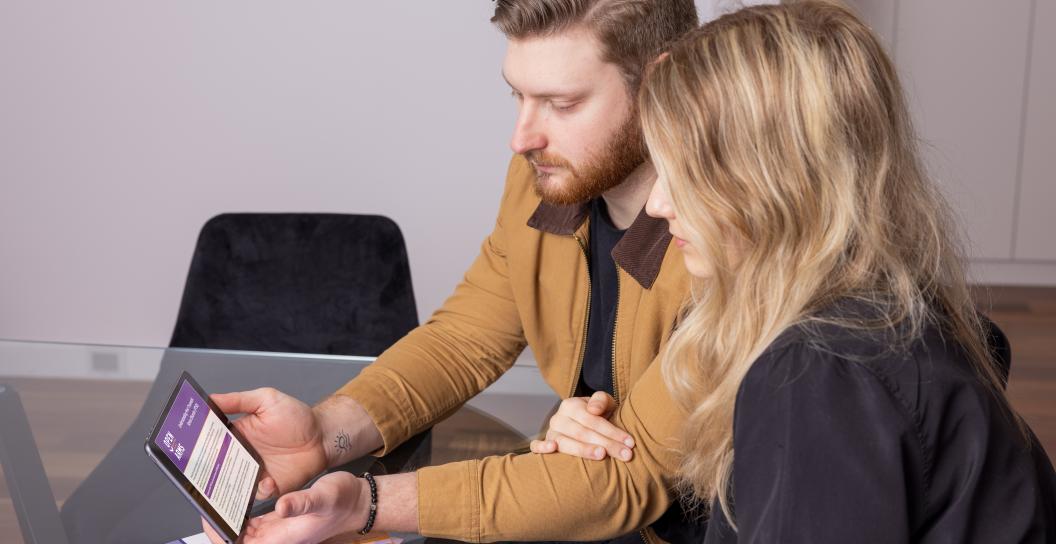 A man and woman look at a tablet with the Open Arms website