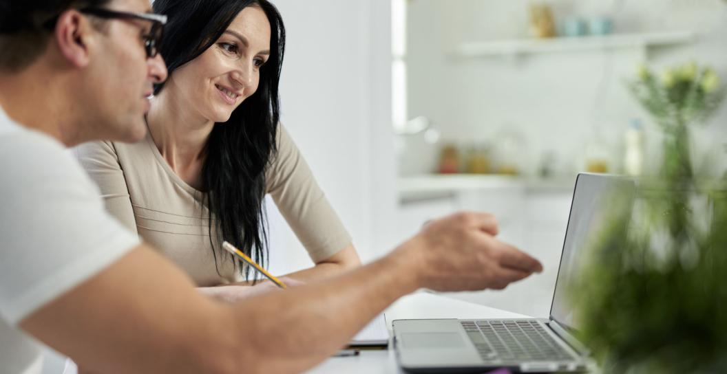 Two people are using an open laptop at a desk
