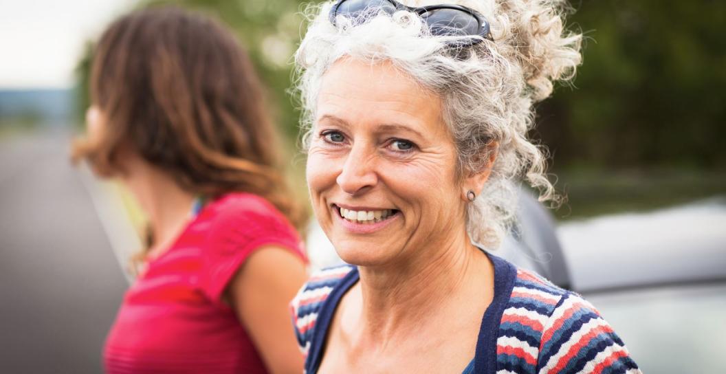 a woman in her 40s or 50s smiles at the camera she has blonde-grey curly hair in a ponytail. there is a younger woman next to her, looking in the other direction.