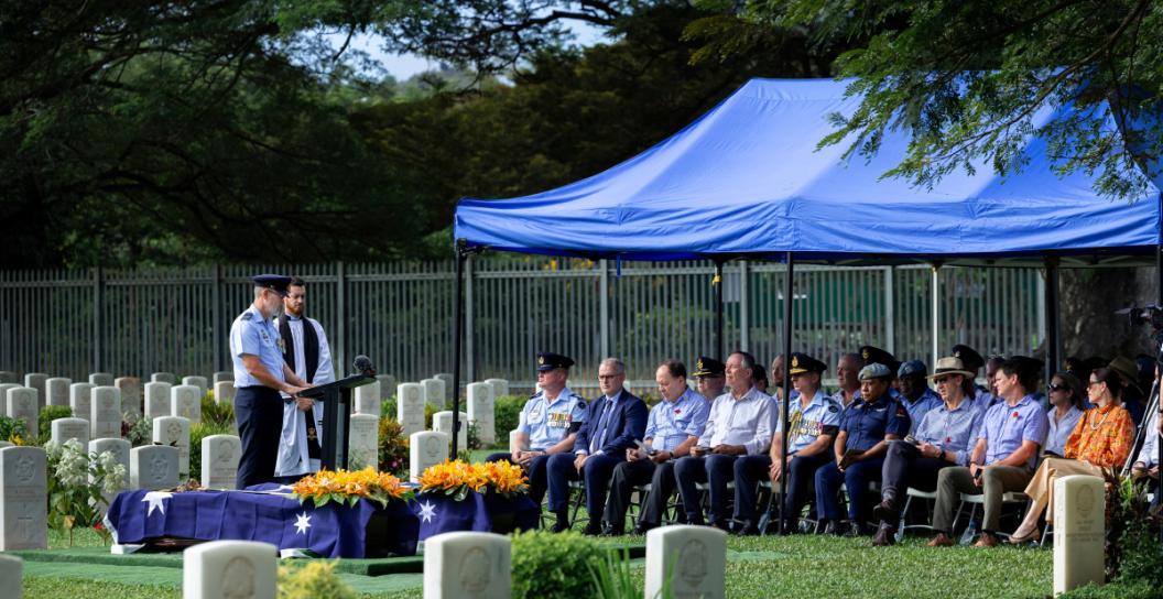 RAAF officer stands at lectern in front of dozens of people under marquee in cemetery.