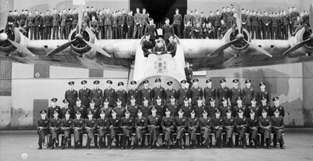 Black and white photo of about sixty air force personnel posing on and in front of a large aircraft