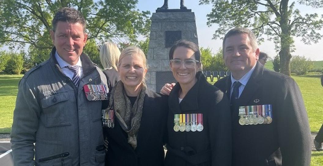 Four people wearing medals posing in front of digger memorial