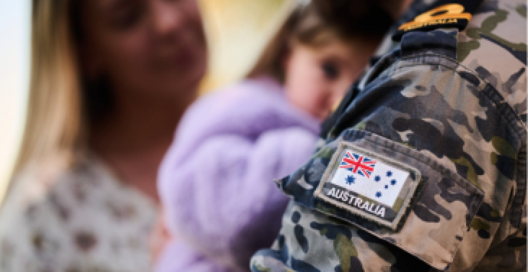 A person in navy uniform holds a young girl in their arms whilst talking to a woman